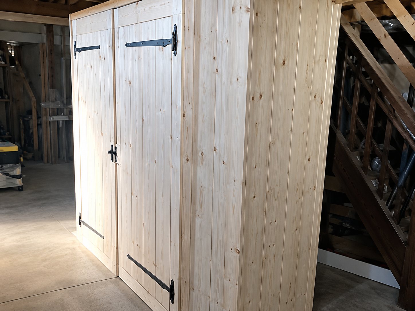 Une cloison en planches de bois clair avec une porte, installée dans un espace aux poutres apparentes.