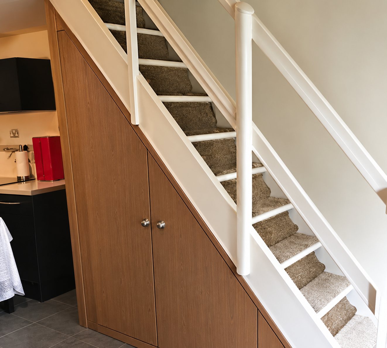 Un escalier blanc à rampe en bois dont le dessous est aménagé avec des placards à portes de bois clair.
