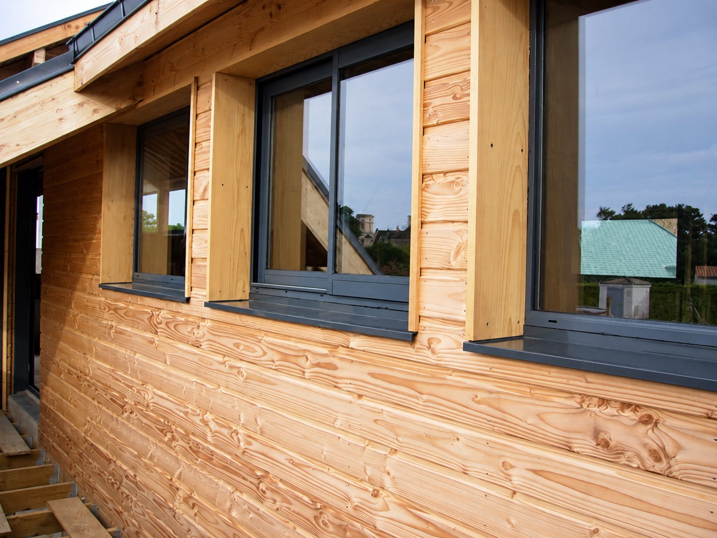 Façade en bardage bois clair avec fenêtres aluminium gris anthracite