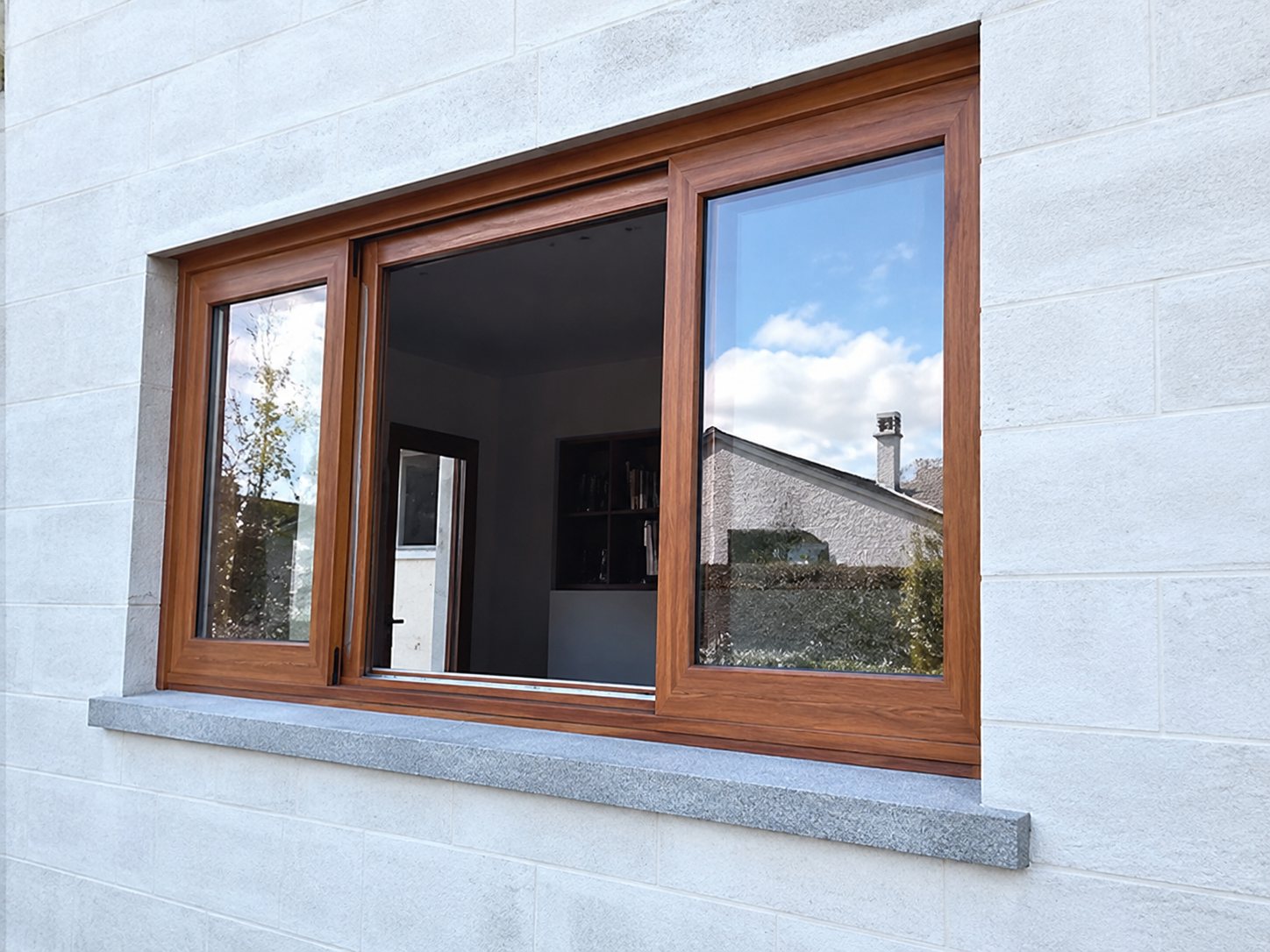 Une fenêtre à cadre en bois brun, équipée de vitrages coulissants, est posée dans un mur de façade clair.