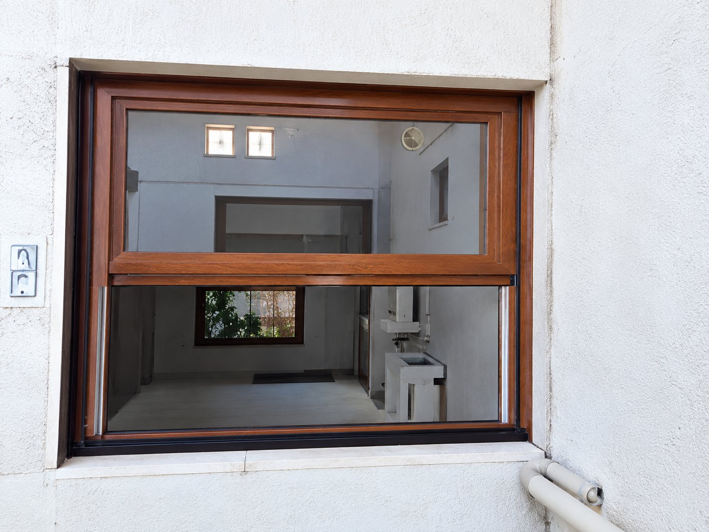 Une grande fenêtre à cadre brun foncé est posée dans un mur clair, laissant entrevoir l'intérieur de la pièce.