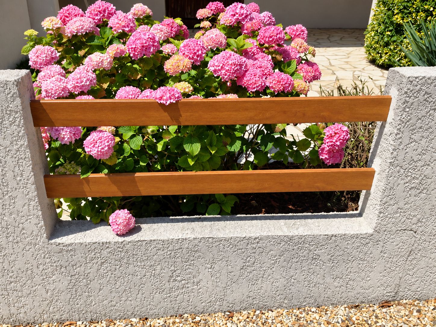 Un muret de clôture en crépi gris orné de deux lames de bois horizontales, derrière lesquelles fleurissent des hortensias roses.