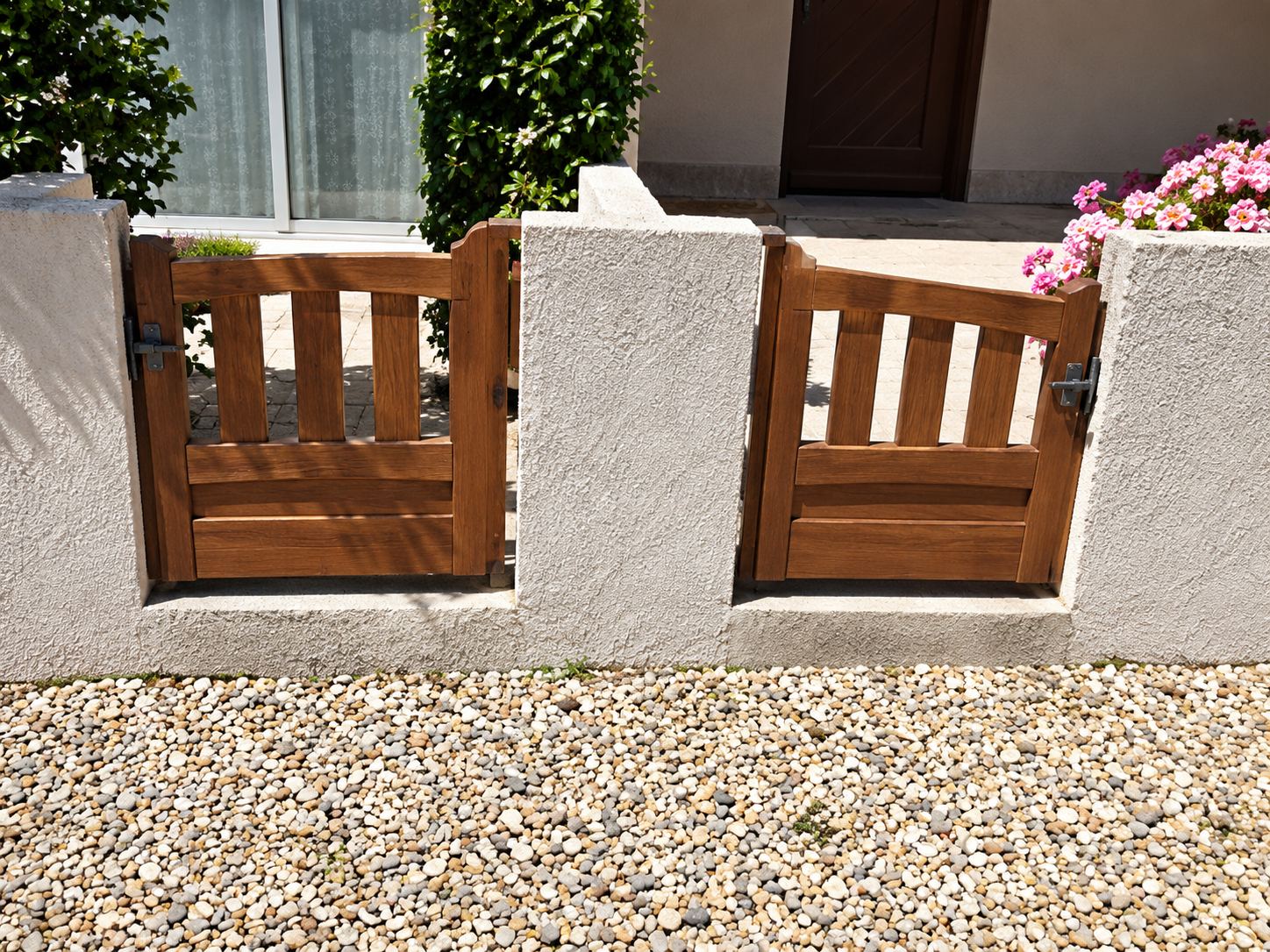Un portillon et un portail en bois à lames verticales sont installés entre des piliers et des murets enduits de couleur beige devant une maison.