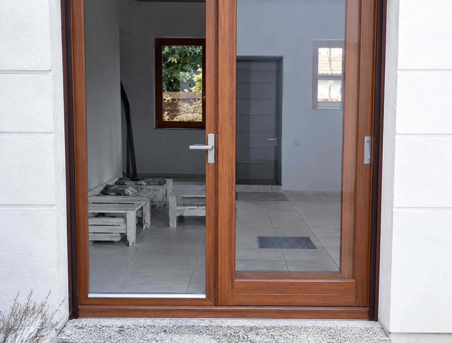 Une porte-fenêtre à double battant avec un cadre en bois et de grandes vitres, installée dans un mur clair et laissant voir l'intérieur d'une pièce.