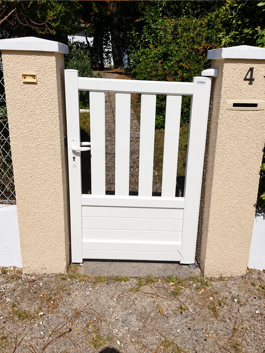 Un portillon blanc à barreaux verticaux et à partie basse pleine est installé entre deux piliers en crépi beige, dont l'un porte le numéro 4.
