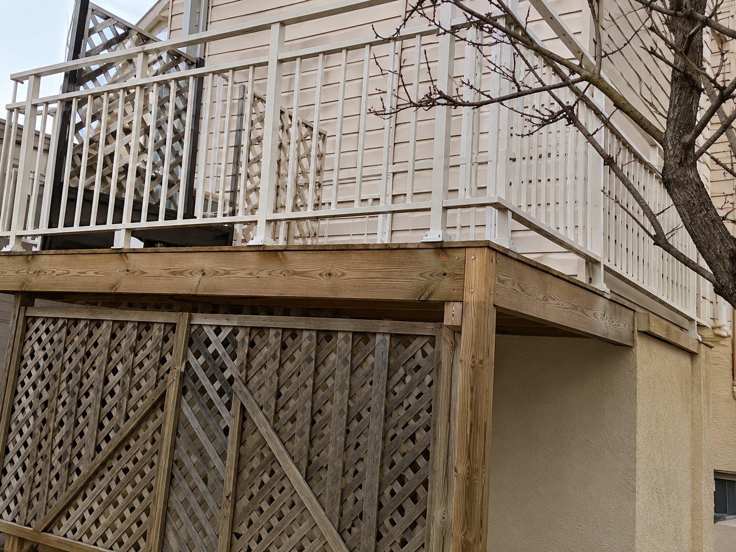 Une terrasse surélevée en bois avec un garde-corps métallique et un treillis, installée contre la façade d'un bâtiment.