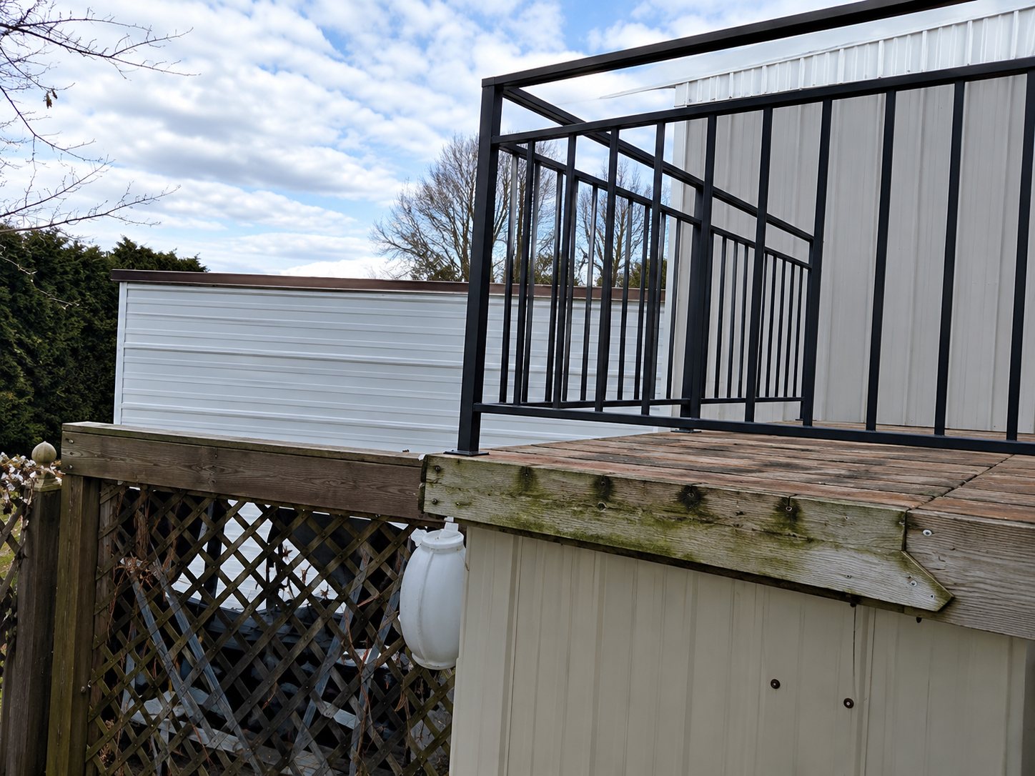 Une terrasse en cours de construction avec un garde-corps métallique noir et des murs blancs sous un ciel nuageux.